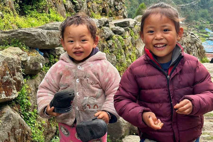 Two smiling Nepali children in winter jackets on mountain trail
